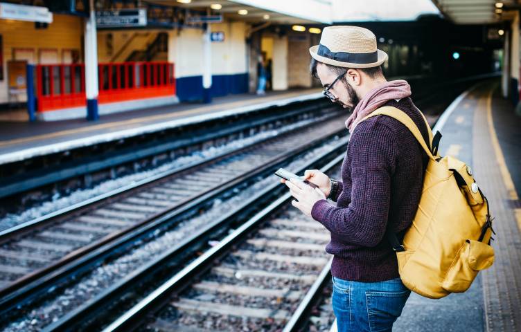 Mies seisoo juna-asemalla ja tutkii käsissään olevaa puhelinta